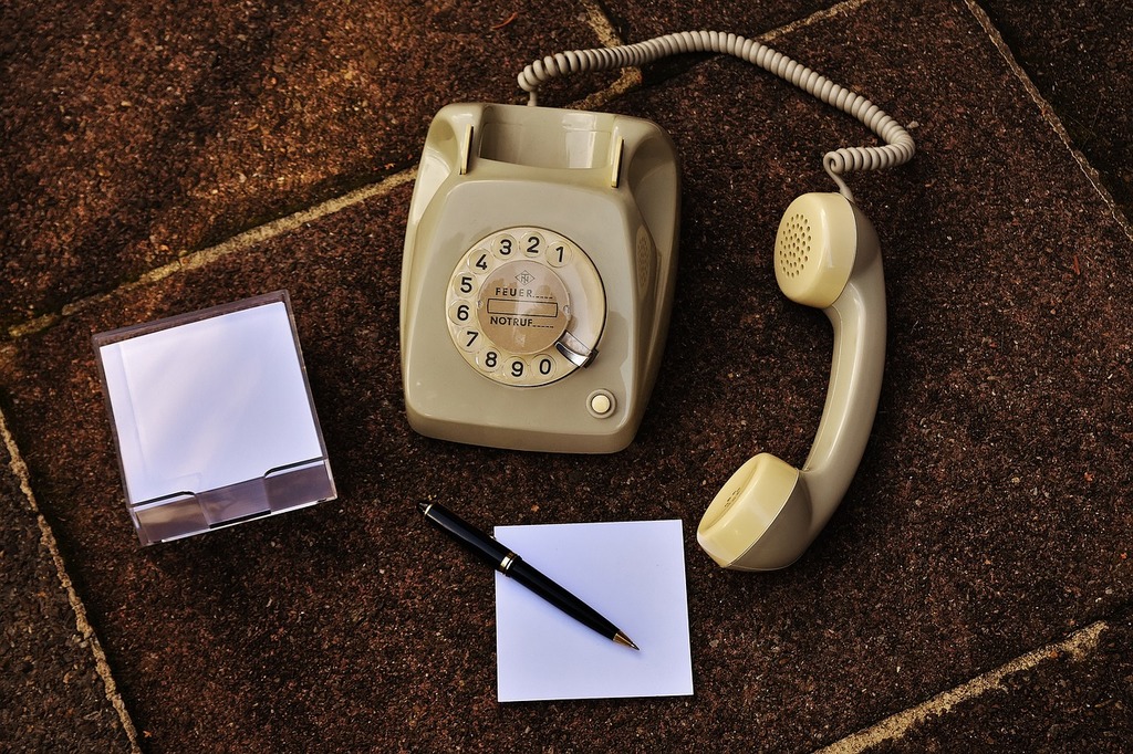 A telephone, a pen, and a notepad on the floor. A telephone, notepad, pen and paper on a carpet. Public domain stock photo.