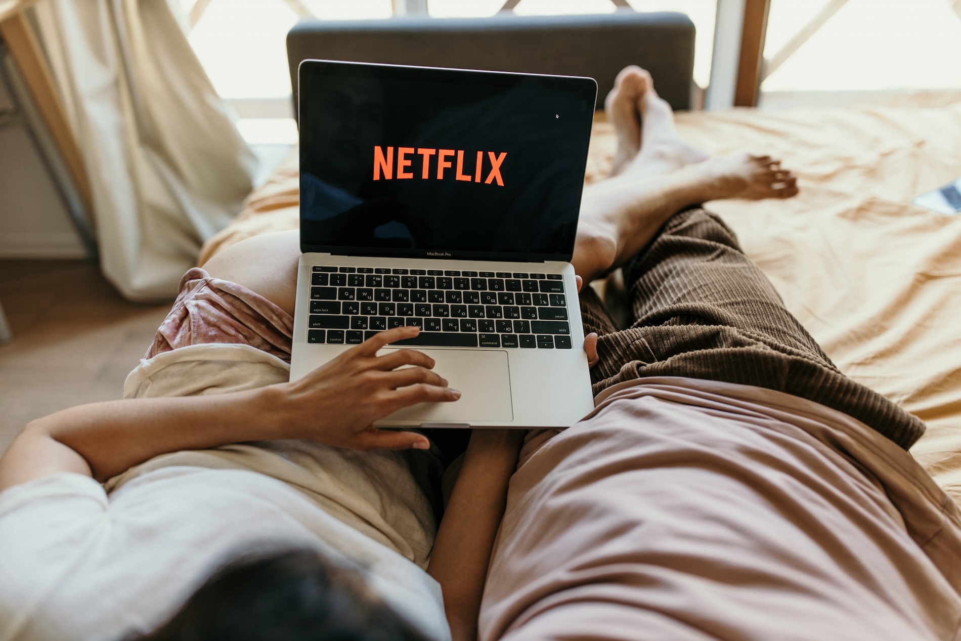 Two people watching Netflix on a laptop in bed
