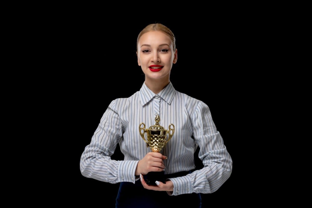 A woman dressed in a striped shirt smiles for a photograph after winning a trophy