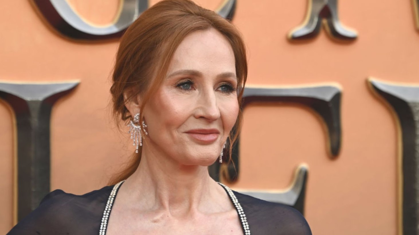 J.K. Rowling wearing elegant diamond earrings and a navy dress with rhinestone trim, and smiling